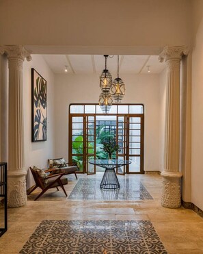 Eine geräumige Lobby mit Glastisch, einer Pendelleuchte und einem großen Fenster mit Blick auf Grünflächen.