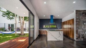 A modern kitchen with a marble island, wooden cabinets, and a blue range hood. - Luxury Pool Home | Sleeps 8 | TV Room + 4 Full Baths (Playa del Carmen)