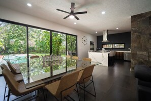 Een moderne keuken met een centraal eiland, een eethoek met een glazen tafel en uitzicht op een zwembad.