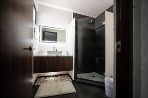 Een moderne badkamer met een glazen douchecabine, een witte wastafel en een marmeren vloer.