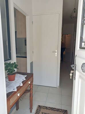 En gang med en lukket dør, en potteplante, en træbænk og en dørmåtte.