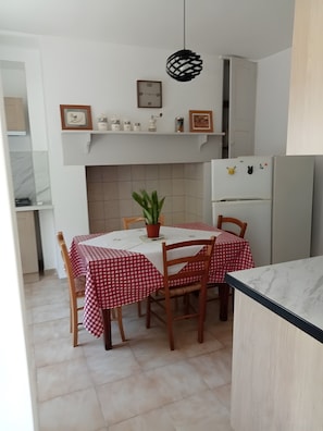 Une cuisine avec une table à manger dressée pour quatre personnes, une plante en pot et un réfrigérateur décoré d’aimants.