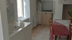 Eine Küche mit Fenster, weißen Schränken, einem Herd und einem Esstisch mit kariertem Tischläufer.