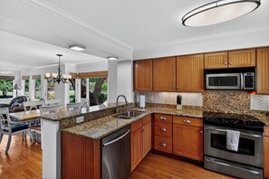 Eine moderne Küche mit Granit-Arbeitsplatten, Edelstahlgeräten, Holzschränken und einem Essbereich mit einer Kronleuchter.