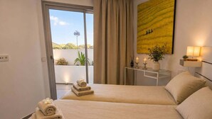 Een hotelkamer met twee bedden, een balkon met uitzicht, een schilderij en een nachtkastje met kaarsen.