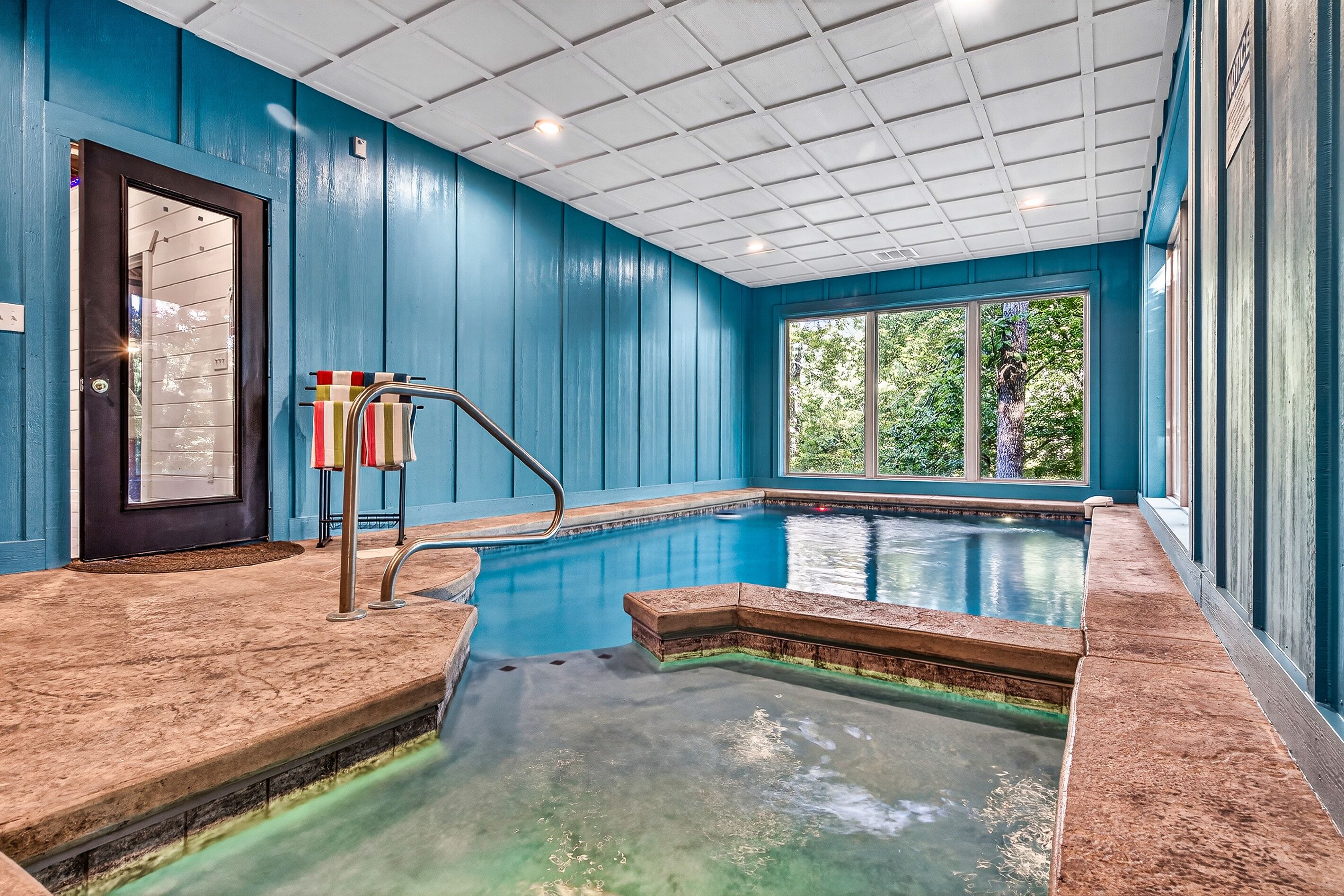 Une piscine intérieure avec vue sur les arbres, une porte et une fenêtre.