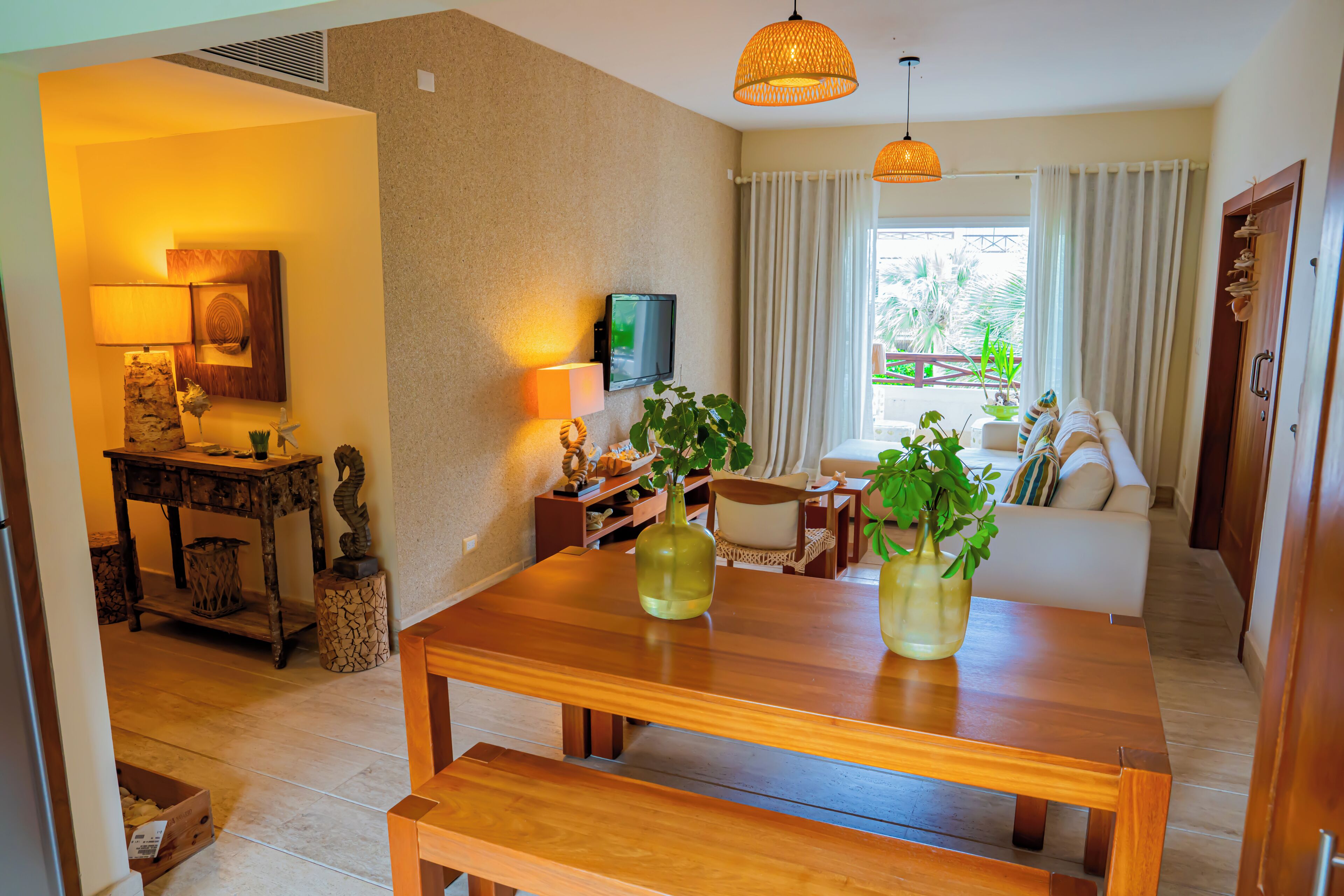 A living room with a wooden table, a sofa, a TV, and a window with curtains.