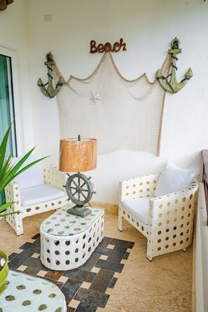Ein Zimmer mit zwei weißen, gepunkteten Stühlen, einem Tisch auf Rädern, einer Lampe und einer Wanddekoration mit der Aufschrift 'Beach'.