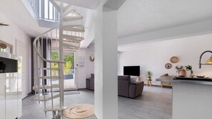 A modern interior with a spiral staircase, a kitchen area, a living room with a sofa, and a dining area with a TV. - Villa "les alizés" garden side, close to the sea (Saint-Raphaël)