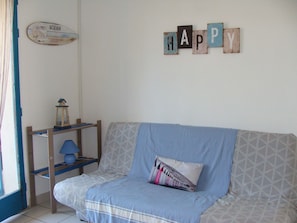 Una habitación con un sofá azul, un estante de madera con una lámpara y un adorno en la pared que dice 'HAPPY'.