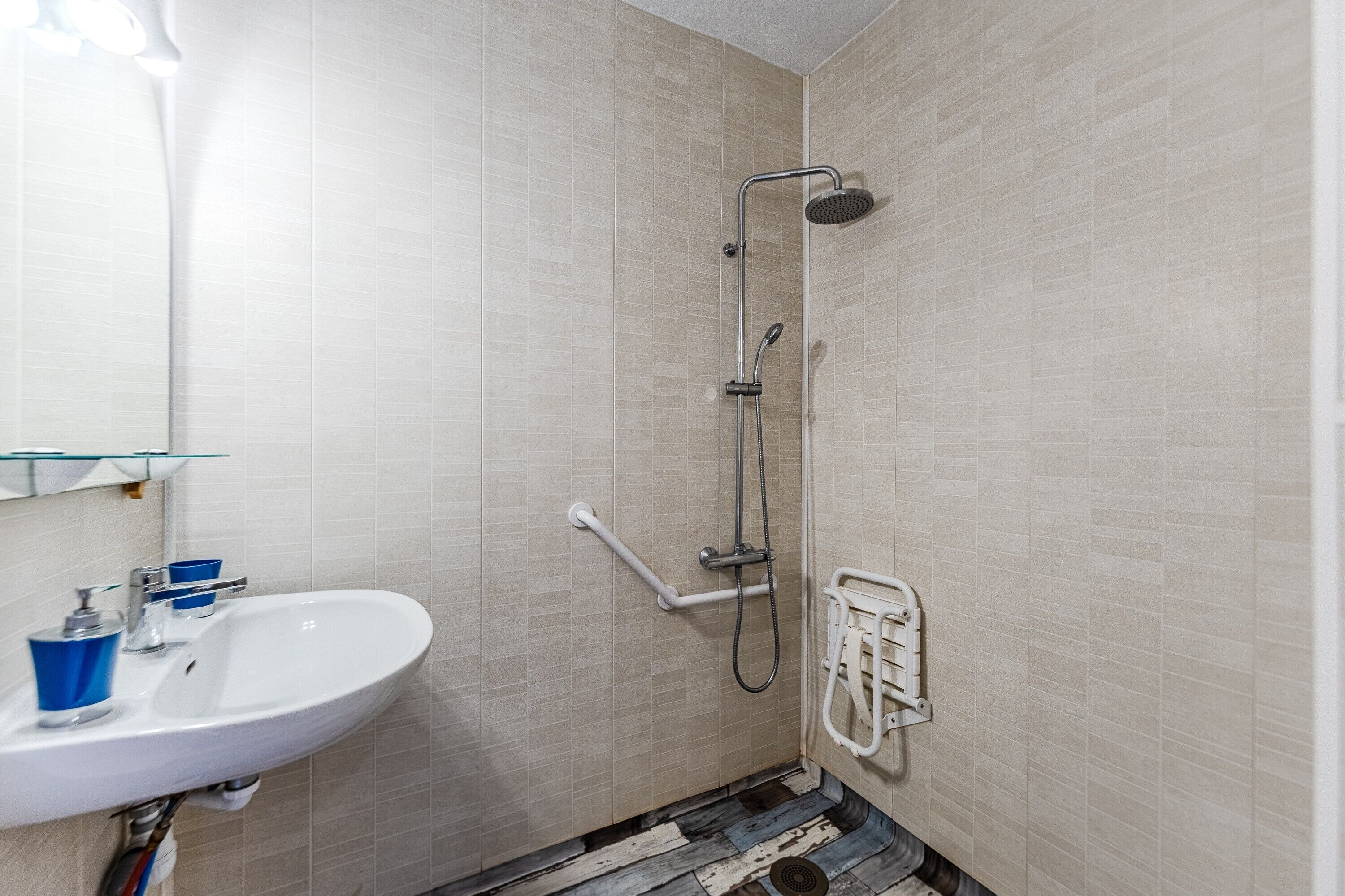Ein Badezimmer mit einem weißen Waschbecken, einer Dusche inklusive Handbrause und einer Haltestange.