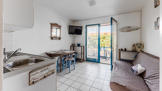 Een kleine keuken met een spoelbak, een eethoek met stoelen, een televisie en een schuifpui naar buiten.