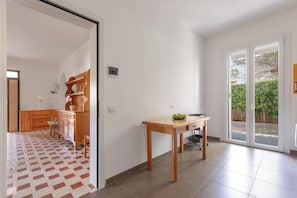 Ein geräumiges Zimmer mit Fliesenboden, einem Holztisch, einem Schrank und einer Glastür zum Außenbereich.