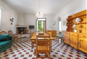 Een eetruimte met een geruite vloer, houten stoelen, een tafel met een schaal, een open haard en een houten kast.