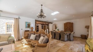 A spacious living room with a large sofa, a dining area with wicker chairs, a chandelier, and a stone wall. - MASTRU BELLU (BONIFACIO)