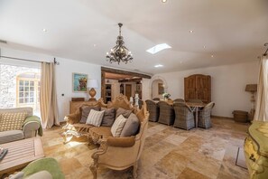 Ein geräumiges Wohnzimmer mit einer großen Couch, einem Essbereich mit Korbstühlen, einer Chandelier und einer Steinwand.