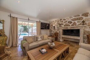 Ein Wohnzimmer mit Kamin aus Stein, einer Couch, einem Couchtisch und Blick auf einen Pool.
