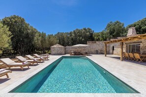 A rectangular swimming pool with lounge chairs and a stone building with a chimney. - MASTRU BELLU (BONIFACIO)