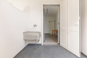 Een smalle gang met een wastafel, een deur en een tafel met een kom.
