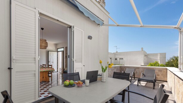 Une terrasse extérieure avec une table, des chaises et un ordinateur portable.