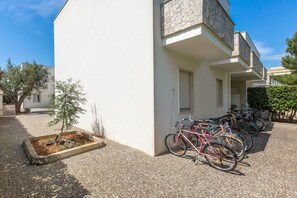 Ein Gebäude mit weißer Fassade, ein kleiner Baum in einem Pflanzkübel und Fahrräder, die davor abgestellt sind.