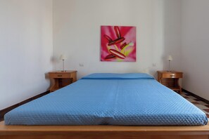 Ein Zimmer mit einem Bett, zwei Nachttischen, einer Lampe auf jedem Nachttisch und einem Bild an der Wand.