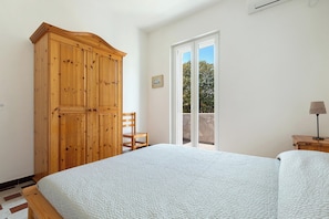 A bedroom with a bed, wooden wardrobe, chair, and a view through a sliding door.