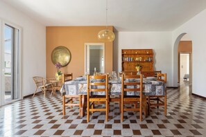 A dining area with a checkered floor, a wooden dining table, chairs, a hanging light fixture, and a bookshelf.