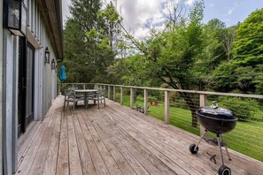 A wooden deck with a table and chairs, a barbecue grill, and a view of a green landscape.