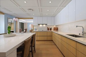 A modern kitchen with a marble countertop, wooden cabinets, and a central island with seating. - Hapuna Beach Residences B31 Three Bedroom (Kamuela)