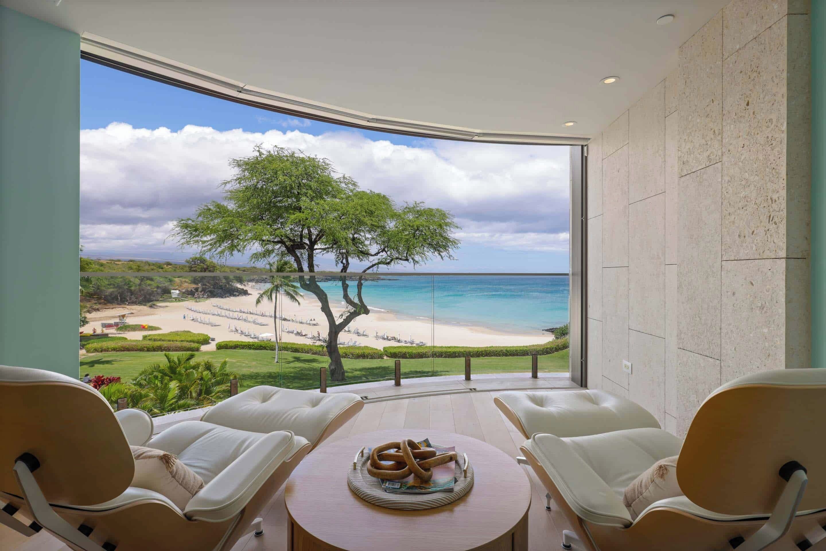 Un balcon donnant sur une plage et l’océan, deux chaises blanches et une table ronde avec un plateau.