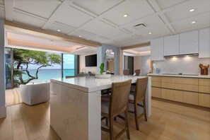 A modern kitchen with a marble island, wooden chairs, and a view of the ocean. - Hapuna Beach Residences B31 Three Bedroom (Kamuela)