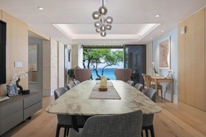 A modern dining room with a marble table, grey chairs, a chandelier, and a view of the sea. - Hapuna Beach Residences B31 Three Bedroom (Kamuela)