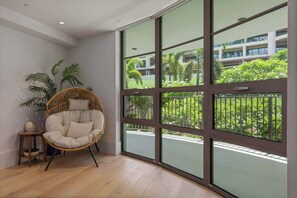 Una habitación con un ventanal grande, una silla de mimbre y una mesita pequeña.