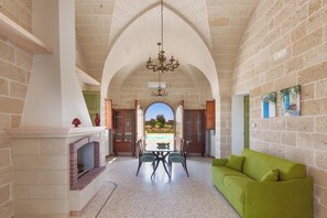 Un espace repas comprenant une table et des chaises, une cheminée et une vue sur l’extérieur, accessible par un passage en arc de cercle.