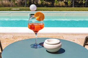 Een glas met een sinaasappelschijfje op een tafel bij een zwembad.
