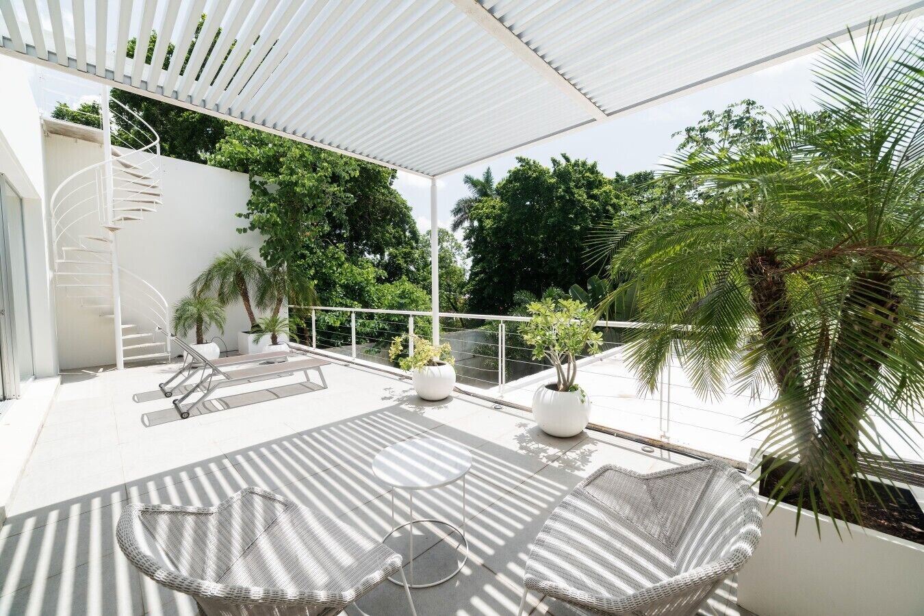 Une terrasse extérieure moderne, dotée d’un escalier en colimaçon, de chaises longues et de plantes en pot.