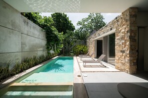 Ein moderner Poolbereich im Freien mit einer Betonwand, einer Steinsäule und Liegestühlen.