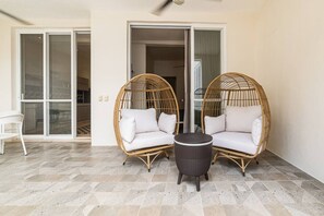 Ein Balkon mit zwei Korbstühlen, einem kleinen runden Tisch und einem weißen Stuhl.