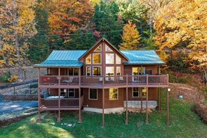 Eine zweistöckige Holzhütte mit Balkon, umgeben von herbstlichem Laub.