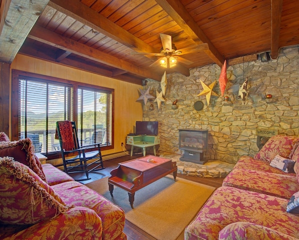 Ein gemütliches Wohnzimmer mit Steinwand, Kamin, Fernseher und bequemen Sitzmöglichkeiten.