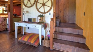 Interior de madera con una escalera, una mesa blanca con cajones y dos grandes ruedas de madera en la pared.
