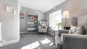 A living room with a bookshelf, a chair, a lamp, and a window. - greenhead hotel (Greenhead)