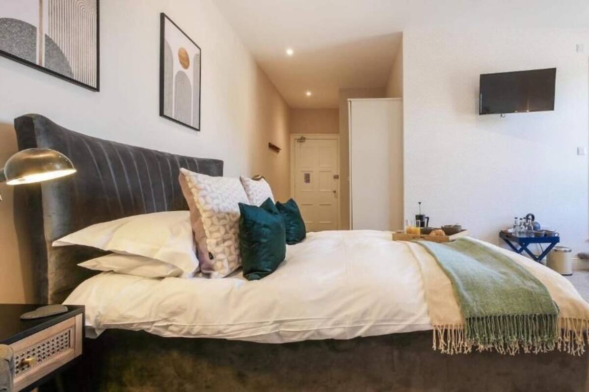 Un dormitori amb llit, una làmpada de nit, un televisor a la paret i una porta que dona a una altra habitació.