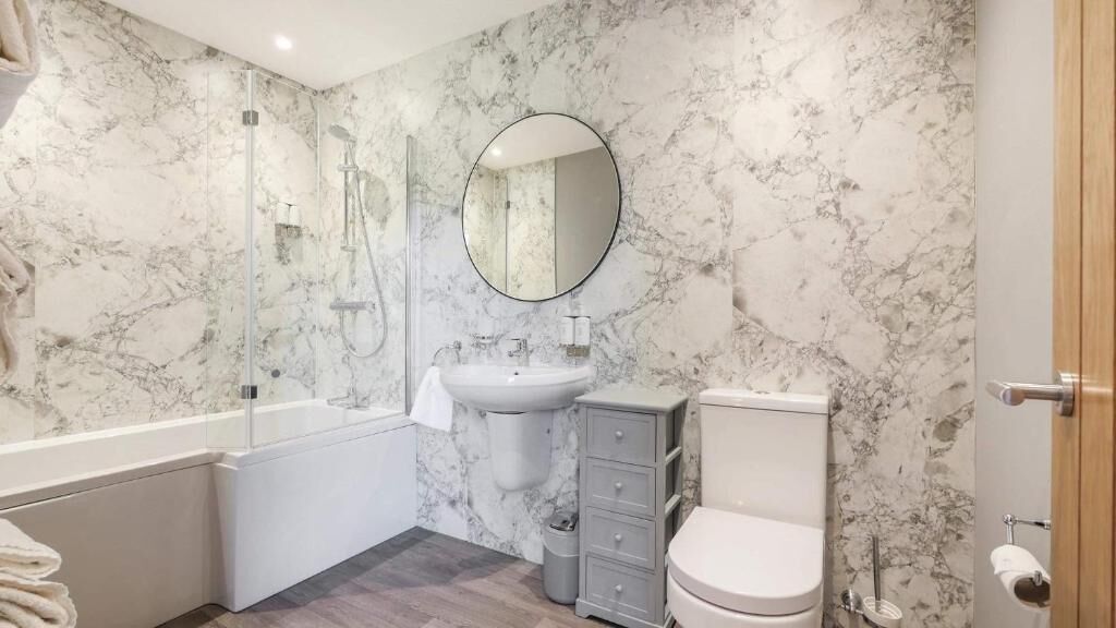 Un baño con pared de mármol, un lavabo, un inodoro, una ducha y un espejo.
