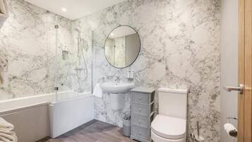 A bathroom with a marble wall, a sink, a toilet, a shower, and a mirror.
