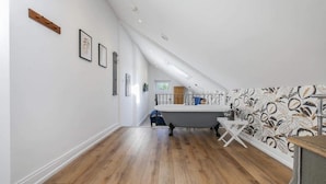 A room with a sloped ceiling, wooden flooring, a white bathtub, and a wall with a floral pattern. - greenhead hotel (Greenhead)