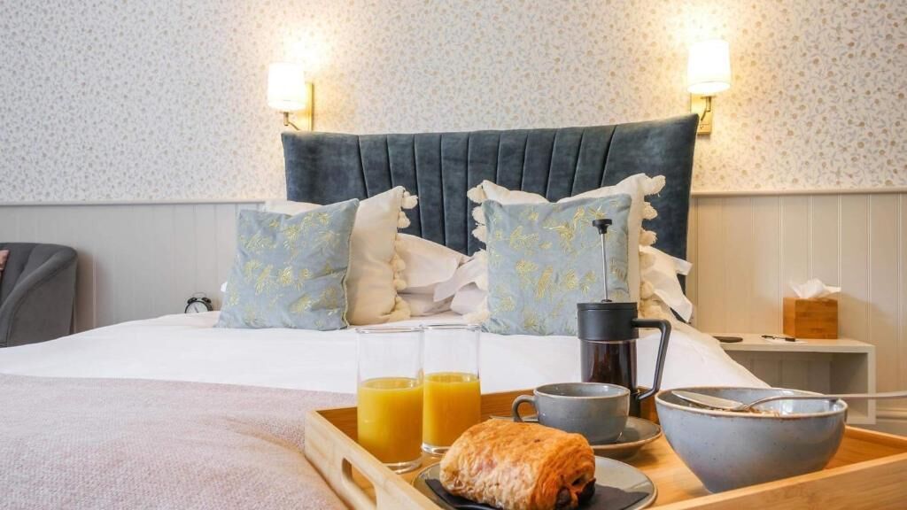 Una cama bien hecha con almohadas, una bandeja con alimentos para el desayuno y una cafetera.