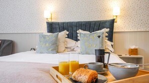 Una cama bien hecha con almohadas, una bandeja con alimentos para el desayuno y una cafetera.