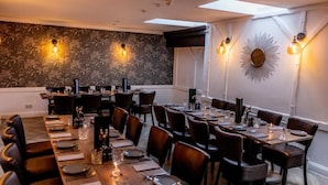 A dining area with multiple tables set for a meal, a decorative wall with a sunburst mirror, and wall-mounted lighting. - greenhead hotel (Greenhead)